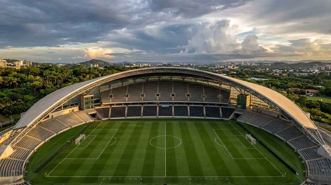 Open-air football stadium under a bright sky with partial cloud, green pitch and covered stands